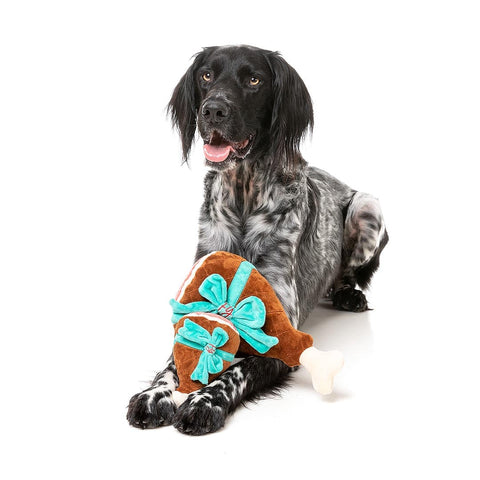 Hond ligt met een pluche kerstham als hondenspeeltje tussen de voorpoten