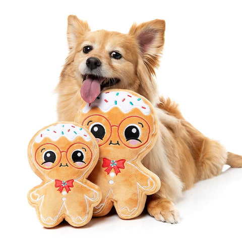 Hond zit achter een groot en klein pluche peperkoekfiguur als hondenspeeltjes