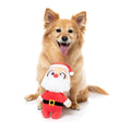 Hond zit achter een pluche kerstman als hondenspeeltje met rode muts en witte baard