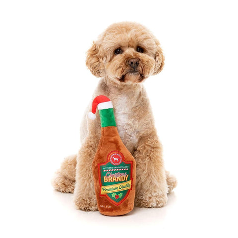 FuzzYard Christmas Brandy – pluche hondenspeeltje in de vorm van een kerstfles met pieper, bruine hond poseert vrolijk met speeltje