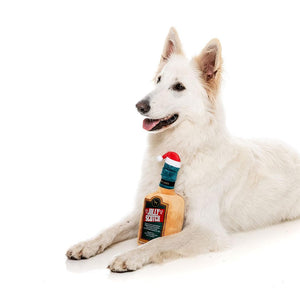 FuzzYard Xmas Jolly Scotch – hond ligt met pluche hondenspeeltje in de vorm van een whiskyfles met kerstmuts
