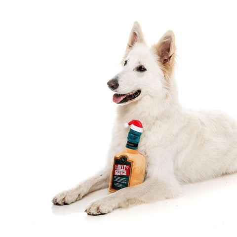 FuzzYard Xmas Jolly Scotch – hond ligt met pluche hondenspeeltje in de vorm van een whiskyfles met kerstmuts