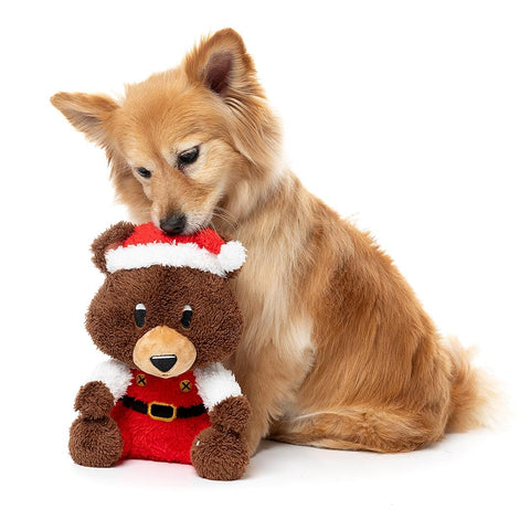 Hond zit achter een bruine pluche beer als hondenspeeltje in kerstpak
